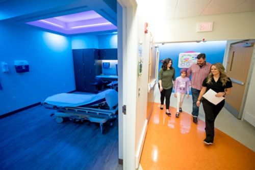 Paciente de câncer pediátrico anda para a sala de ultrassom com pai, técnico de ultrassom e especialista em bem-estar infantil