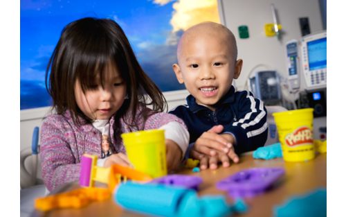 Pediatric cancer patient plays with modeling clay in a hospital bed with his sister