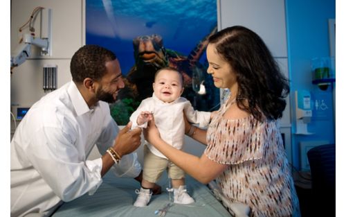 Young child standing with parents on either side holding them up.