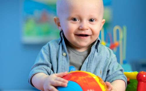 Young child holding onto a toy ball and smiling at the camera.