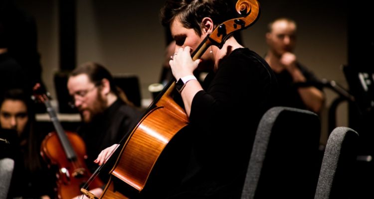 Woman playing cello in foreground with members of symphony in background