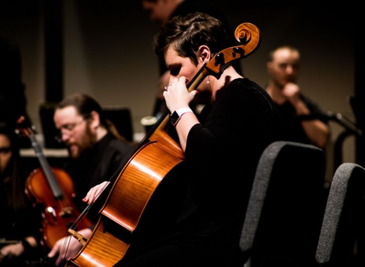 Woman playing cello in foreground with members of symphony in background