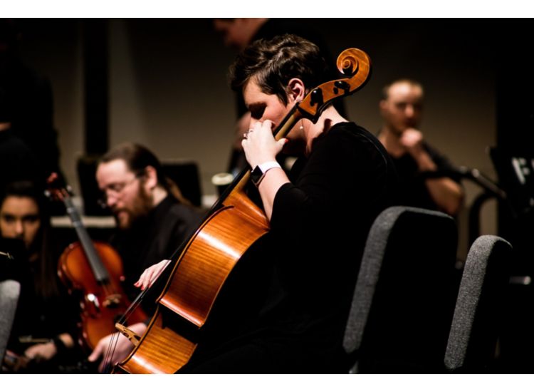 Woman playing cello in foreground with members of symphony in background