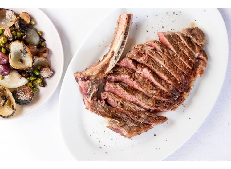 photo of sliced steak net to a big bone next to a plate of vegetables.