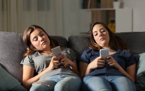 Two girls sit on a couch playing with their phones