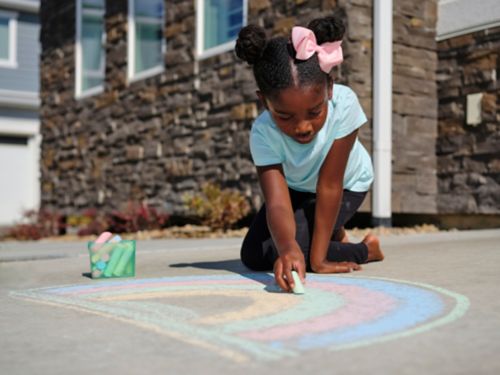 Girl drawing rainbow on sidewalk with chalk