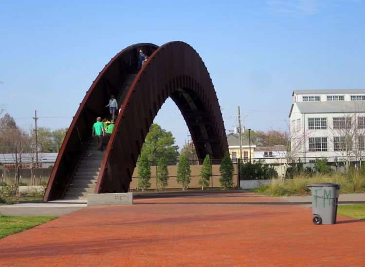 Large arched stairway going over a river in front of a red brick path.