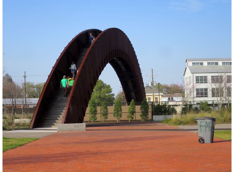 Large arched stairway going over a river in front of a red brick path.