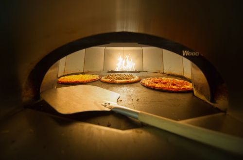 Forno de pizza com três pizzas assando em fogo a lenha