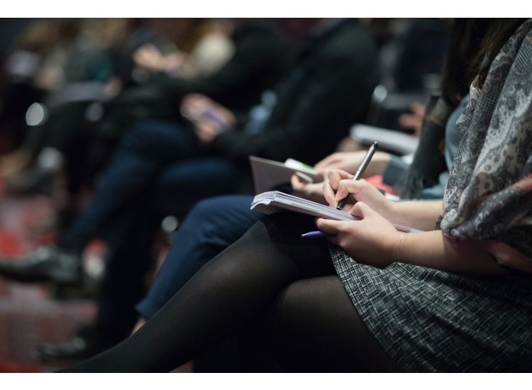 photo of peoples' legs as they sit in a  row of an auditorium