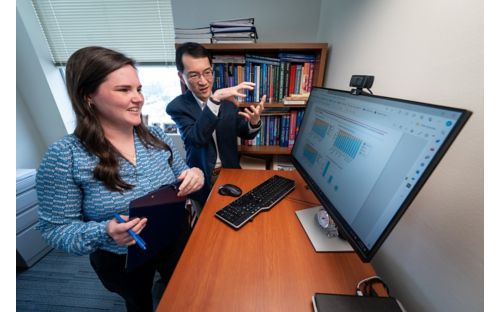 man and woman standing before computer monitor