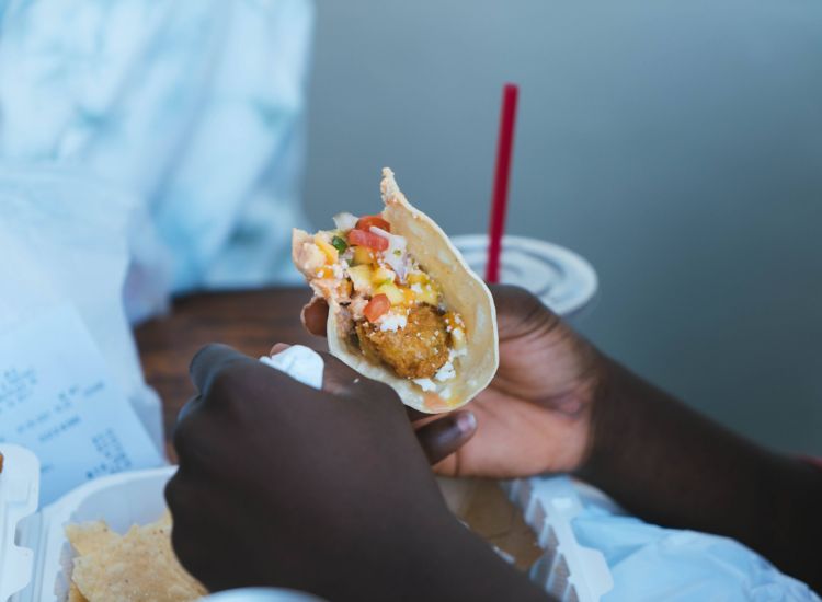 Hands holding fried fish taco with mango salsa
