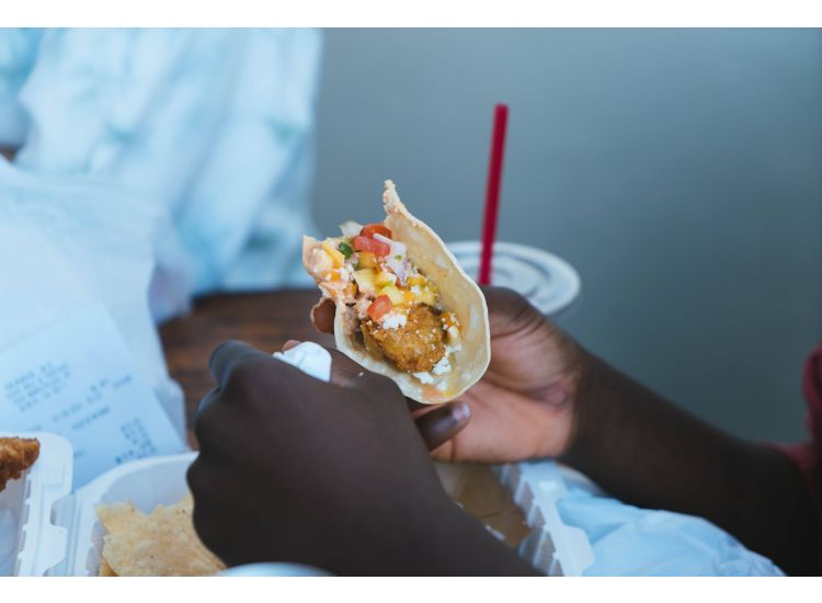 Hands holding fried fish taco with mango salsa