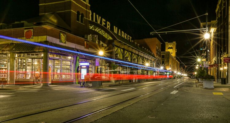 The River Market exterior at night with car lights streaking by.