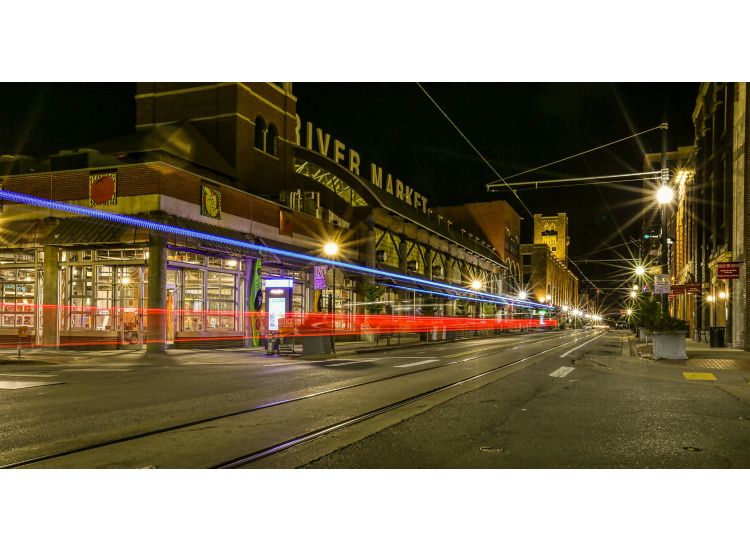 The River Market exterior at night with car lights streaking by.