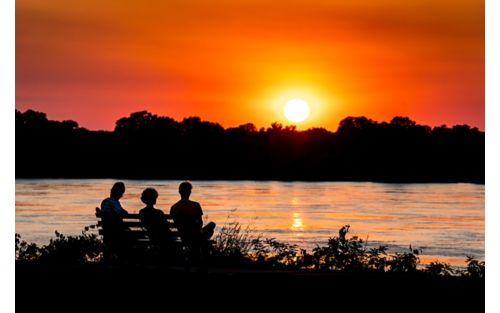 Group of people in silhouette watching sunset near a river