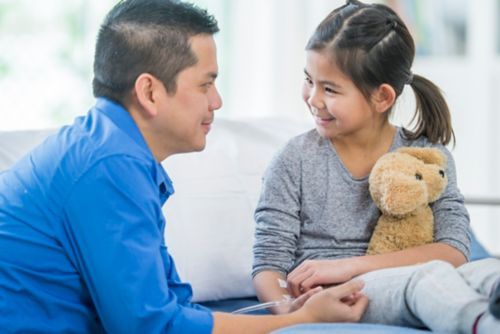 Padre sonriendo a su hija, que sostiene un animal de peluche