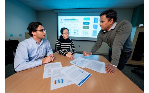 three people at a table, two sitting and one standing