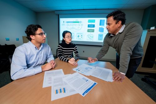 Three people at a table. Two sitting one standing