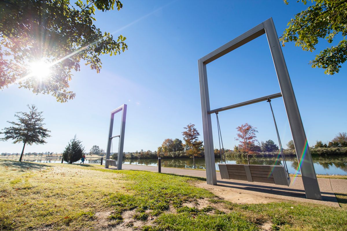 Large swinging bench frames beside a lake on a sunny day. The lake trail at Shelby Farms is about 2.3 miles. 