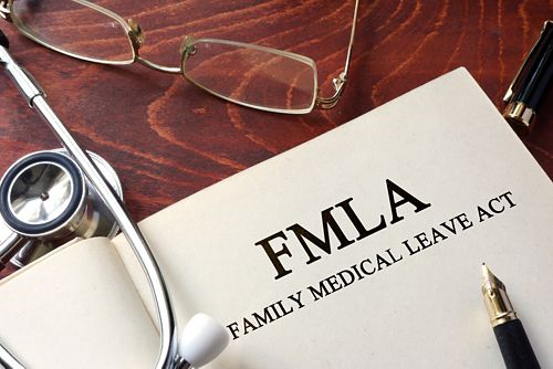 An open book on a table next to a stethoscope and a pair of glasses. The book says FMLA Family Medical Leave Act.