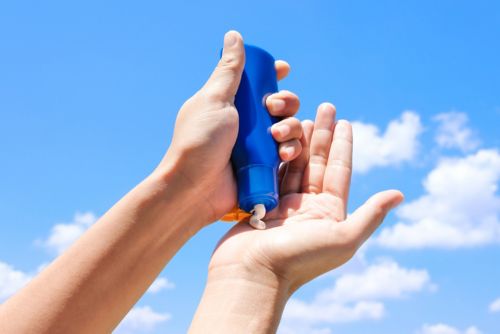 Hands squeezing blue bottle of sunscreen