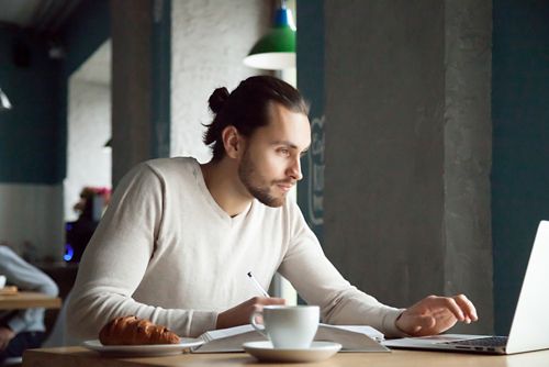 A person using a laptop with a cup of coffee nearby.