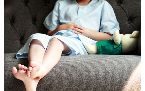 legs of patient kid in blue patient suit sitting on sofa