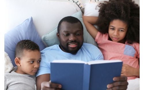 Father reading book to son and daughter in bed.