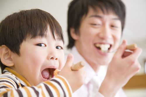 A father and son each taking a bite at the same time.