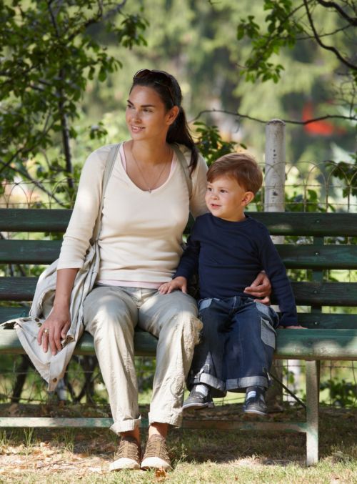 A mother and young son seated on a bench outside.