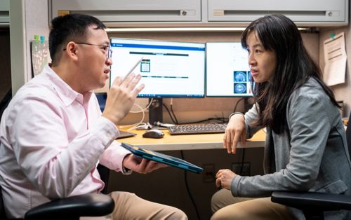 two people talking in front of computer monitors