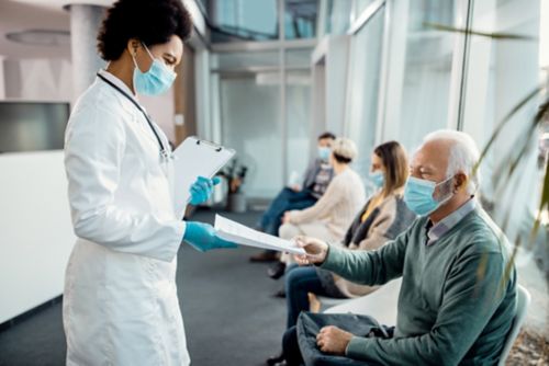 Masked female doctor in white coat handing paperwork to masked patient