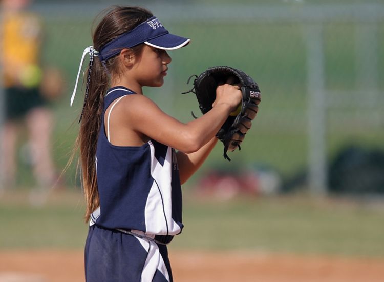 Young girl playing softball with her hand in a baseball glove.
