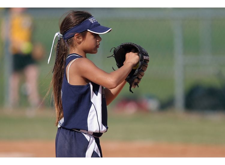 Young girl playing softball with her hand in a baseball glove.