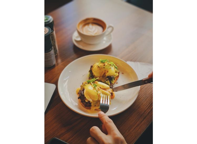 Hands cutting into an eggs benedict.