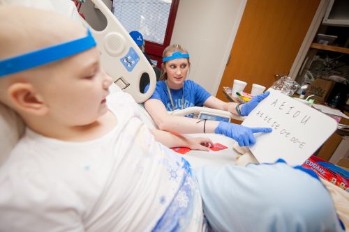 Speech-language pathologist works with pediatric cancer patient at bedside.