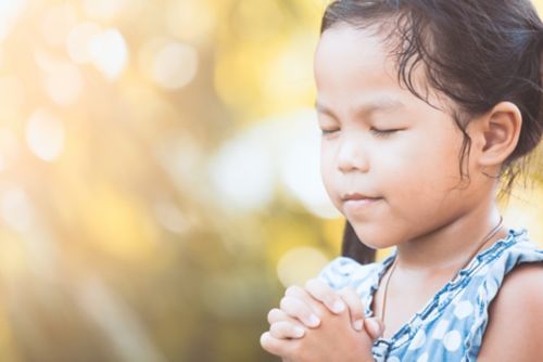 Female child praying with eyes closed.