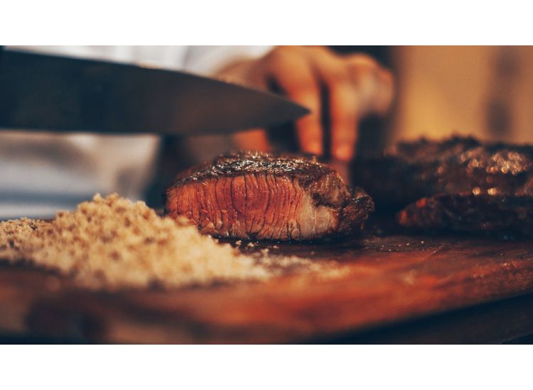 Closeup of steak being sliced with a knife on a cuttingboard. 