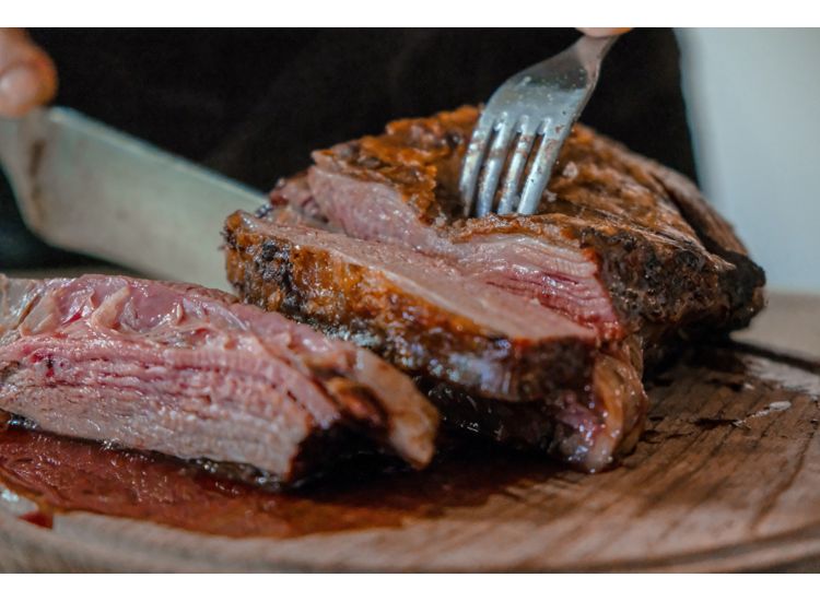 Close up of steak being sliced with fork and knife on a cutting board.