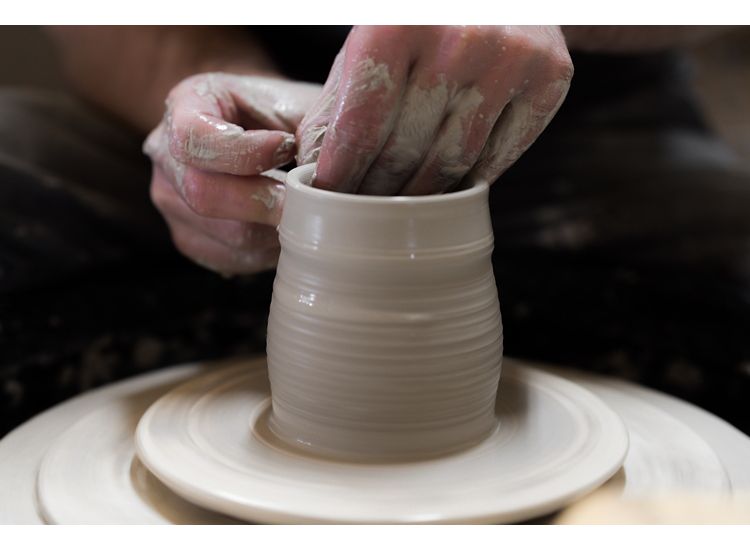 Close up of hands creating a clay vase on a pottery wheel