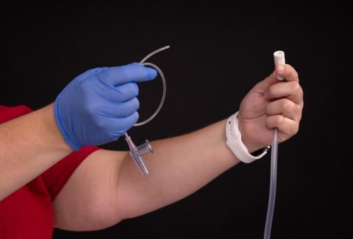 Person with gloved hand holding suction catheter and ungloved hand holding suction tubing