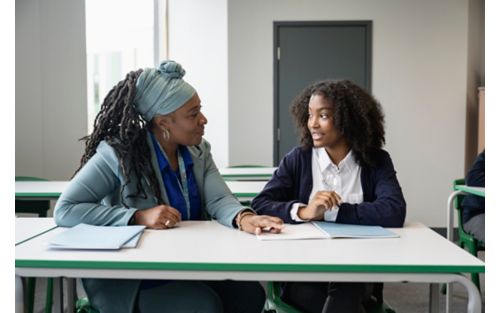 Teacher and student sitting at table, talking to each other