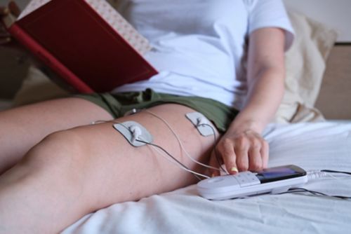 Woman using a TENS unit while reading on a bed
