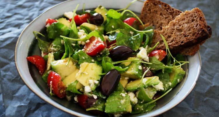 Close up of a salad with olives and tomatoes on a plate.