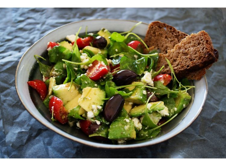 Close up of a salad with olives and tomatoes on a plate.