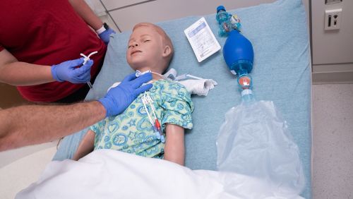 A primary caregiver practicing proper hand placement for a trach on a mannequin,