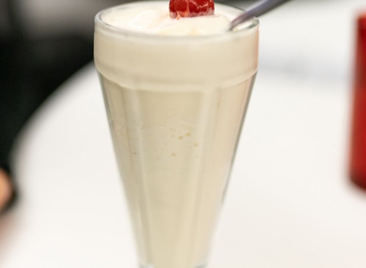 Vanilla milkshake with cherry on top and a spoon.