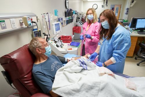 Man donating blood with two nurses near bedside