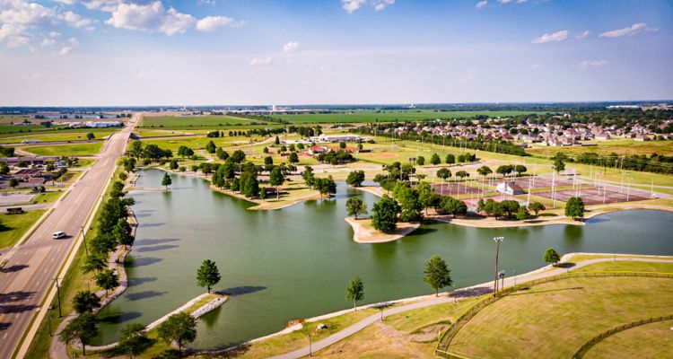 Aerial view of a park with a pond and several sports fields on a sunny day.